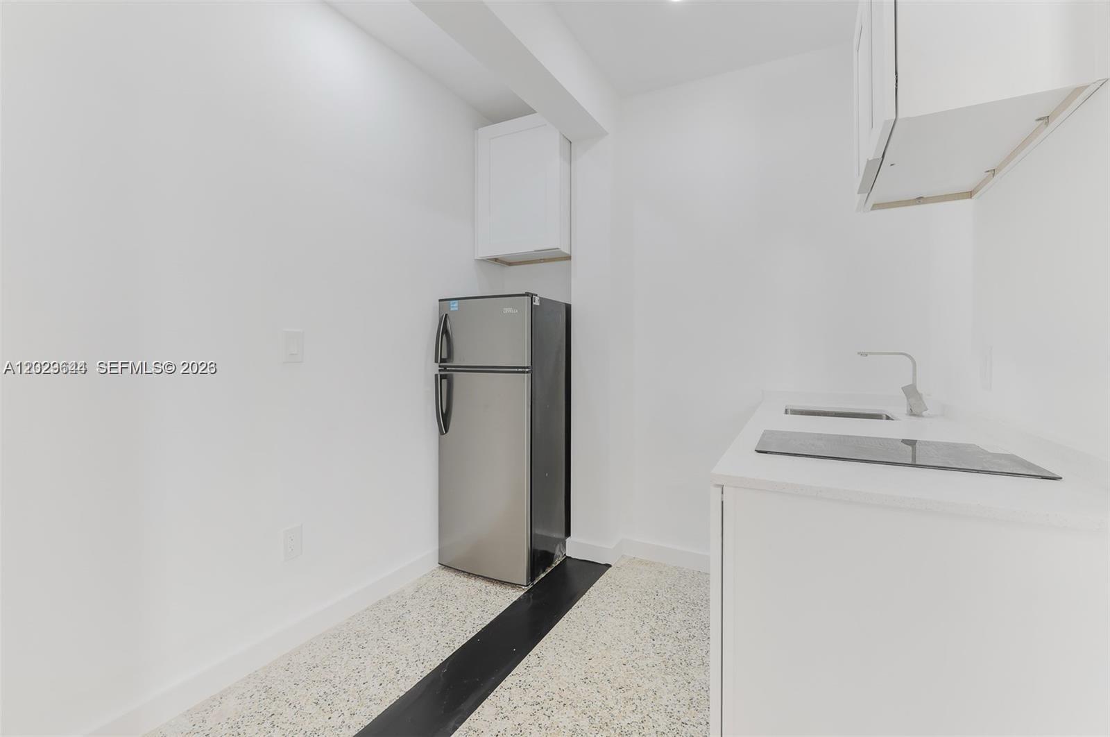 A small kitchen features white cabinets, a stainless steel refrigerator, and a speckled floor — 415 75th St # 4A, Miami Beach FL 33141, MIAMI BEACH, FL