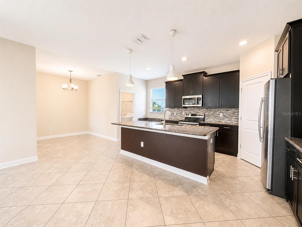 A kitchen with dark cabinets, granite countertops, an island, and tile flooring — 10188 AUTHORS WAY, ORLANDO, FL