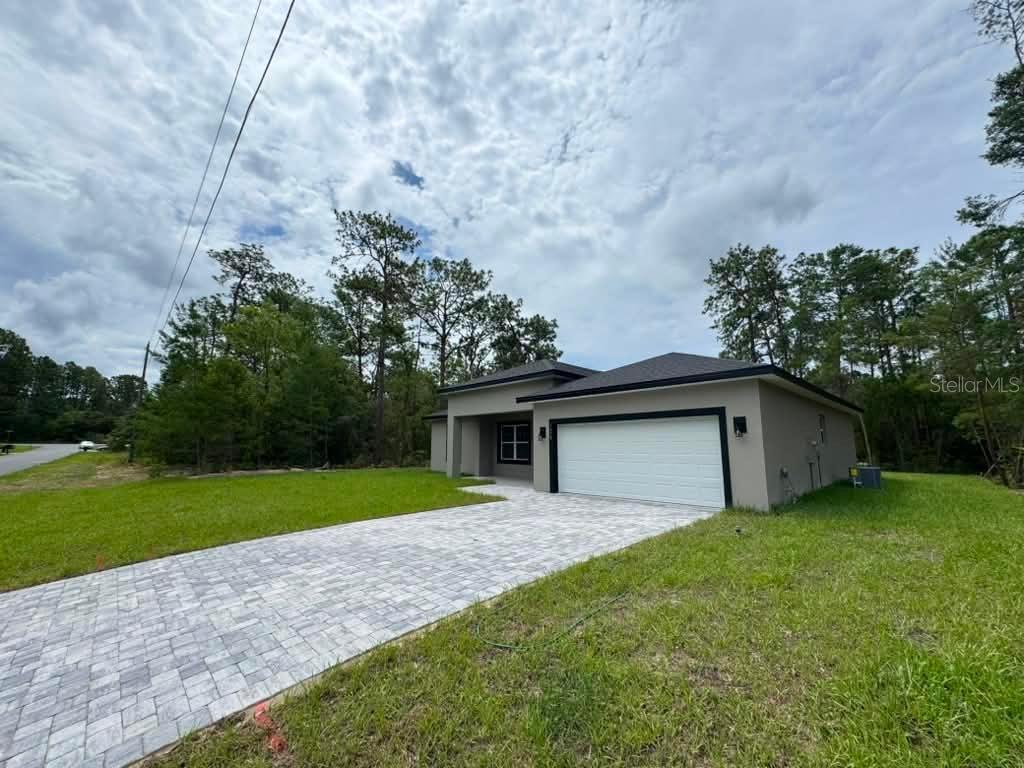 A modern, single-story house with a paved driveway, white garage door, and surrounding wooded area — 1458 W LANDMARK DRIVE, CITRUS SPRINGS, FL