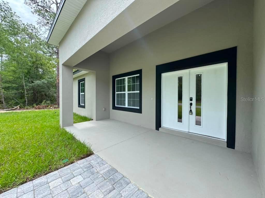 A covered concrete porch features a double front door and windows with black trim — 1458 W LANDMARK DRIVE, CITRUS SPRINGS, FL