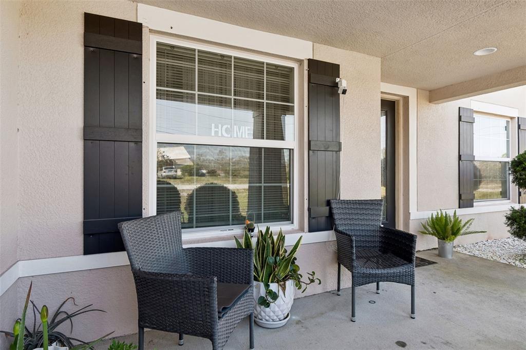 A covered front porch features two wicker chairs, potted plants, and black window shutters — 13046 LINDEN DRIVE, SPRING HILL, FL