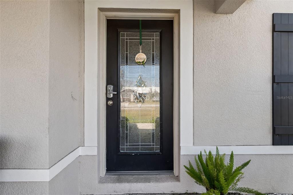 A black front door with a glass insert and a welcome sign sits on a porch — 13046 LINDEN DRIVE, SPRING HILL, FL