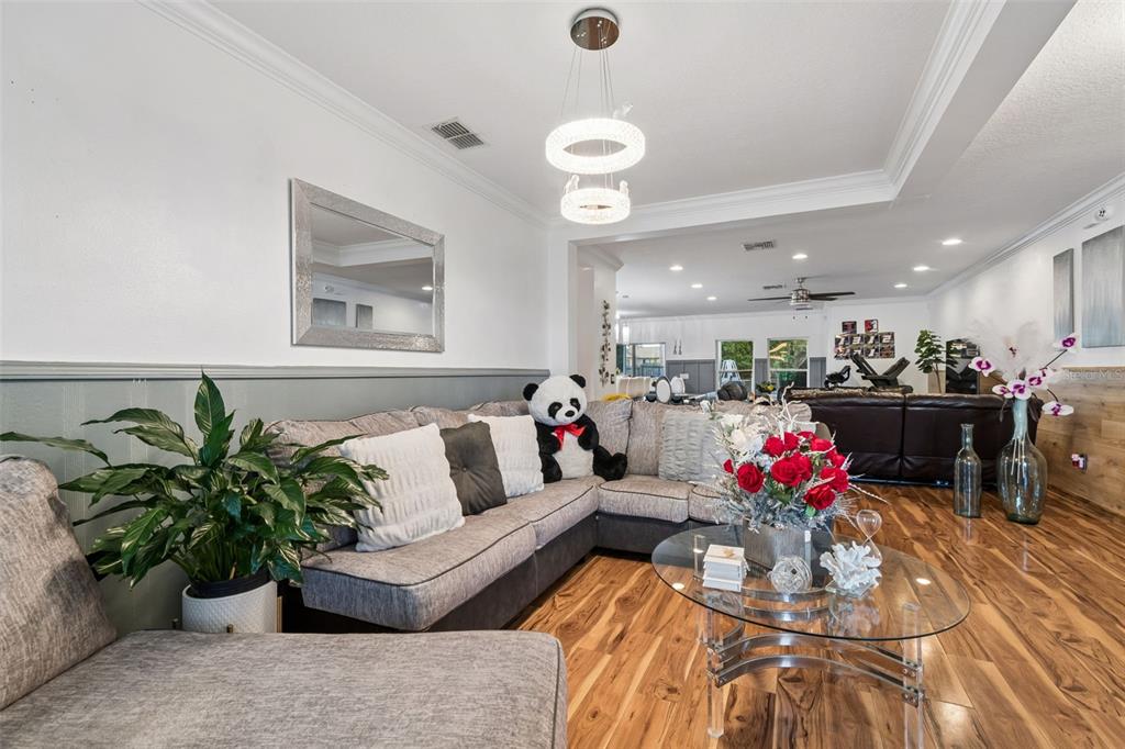 A living room features a grey sectional sofa, wood flooring, a glass coffee table, and a chandelier — 13046 LINDEN DRIVE, SPRING HILL, FL