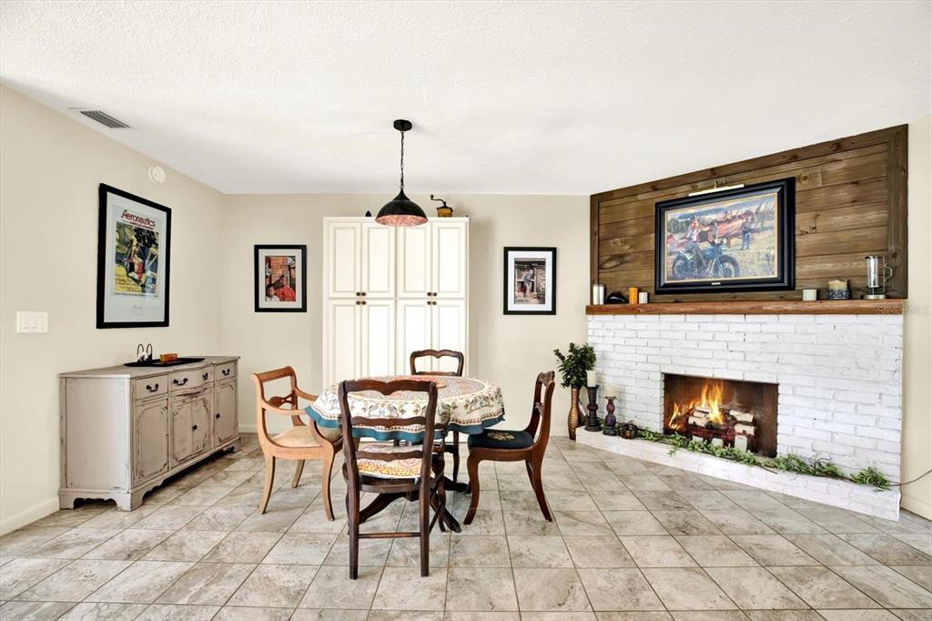 A dining area features a white brick fireplace, a wooden accent wall, and tiled flooring — 4064 N CONCORD DRIVE, CRYSTAL RIVER, FL