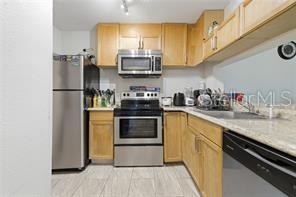 A kitchen features light wood cabinets, stainless steel appliances, and light-colored tile flooring — 5219 VIA HACIENDA CIRCLE UNIT B111, ORLANDO, FL