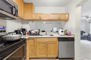 A kitchen features light wood cabinets, stainless steel appliances, and a pass-through window to the living area — 5219 VIA HACIENDA CIRCLE UNIT B111, ORLANDO, FL