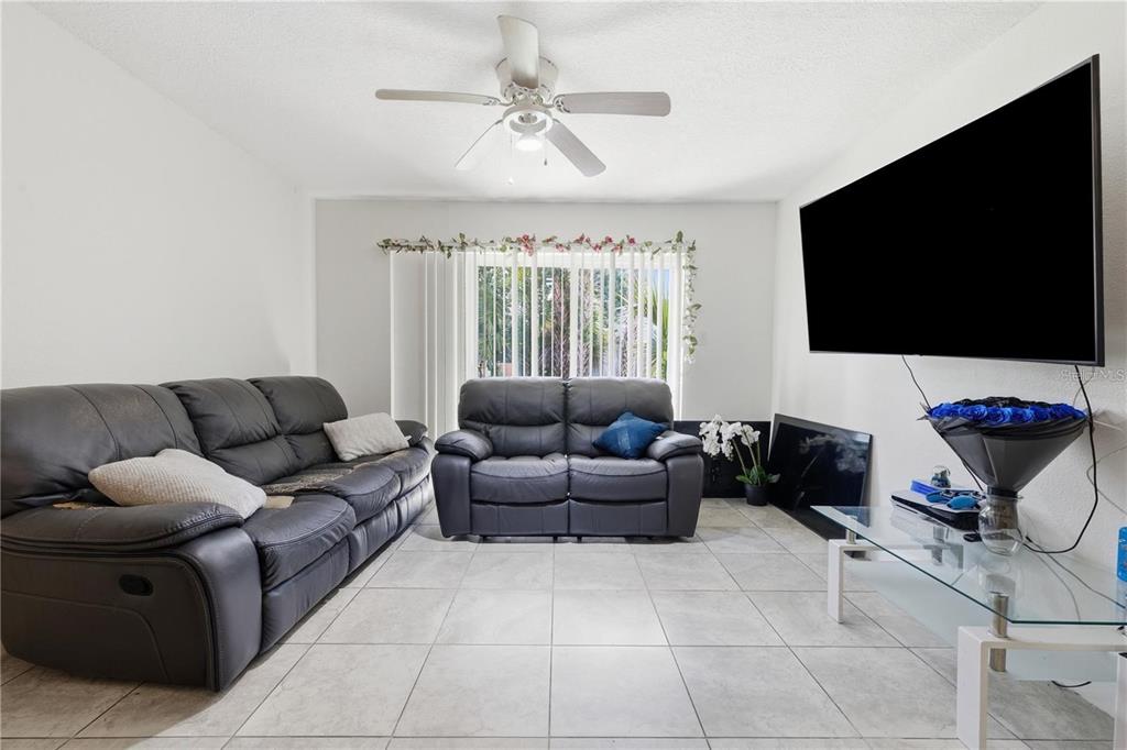 A living room features tile flooring, two dark leather sofas, and a wall-mounted television — 5219 VIA HACIENDA CIRCLE UNIT B111, ORLANDO, FL