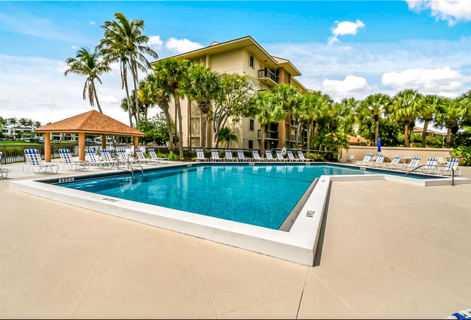 An outdoor swimming pool with a gazebo and lounge chairs sits before a multi-story building — 1701 Marina Isle Way # 103, Jupiter FL 33477, JUPITER, FL