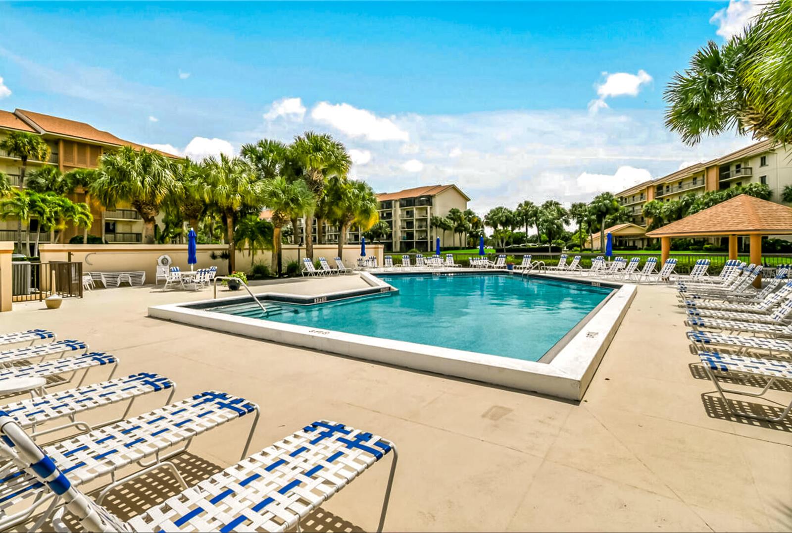 A swimming pool surrounded by lounge chairs and palm trees at an apartment complex — 1701 Marina Isle Way # 103, Jupiter FL 33477, JUPITER, FL