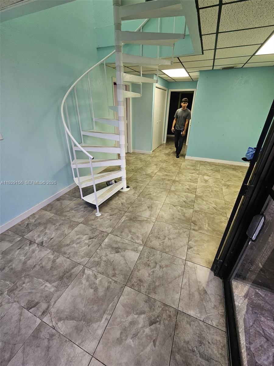 A room with light blue walls, gray tile flooring, and a white metal spiral staircase — 6175 NW 167th St # G18, Hialeah FL 33015, HIALEAH, FL