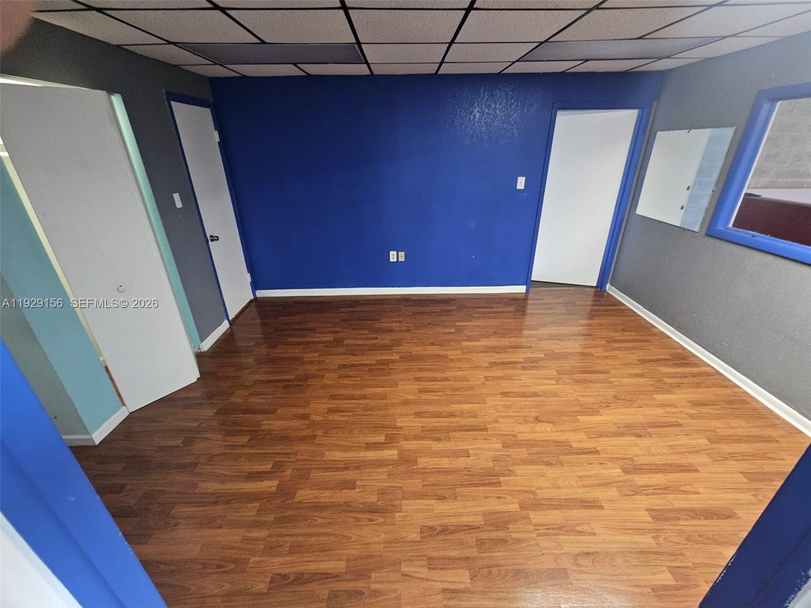 An empty room features wood-look flooring, a blue accent wall, and a drop ceiling — 6175 NW 167th St # G18, Hialeah FL 33015, HIALEAH, FL