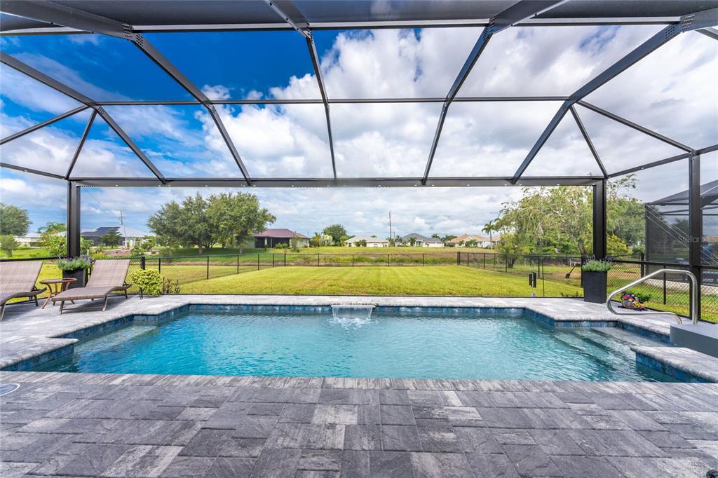 A screened-in patio features a rectangular swimming pool with a waterfall and stone pavers — 940 BOUNDARY BOULEVARD, ROTONDA WEST, FL