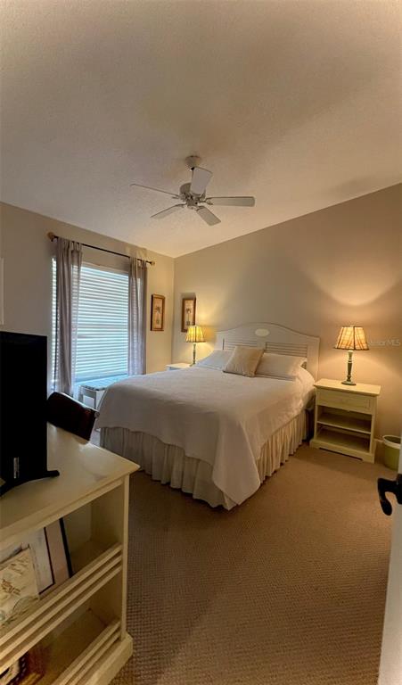 A bedroom features a white bed, a ceiling fan, and a wooden nightstand with a lamp — 4570 WEYBRIDGE UNIT 32, SARASOTA, FL