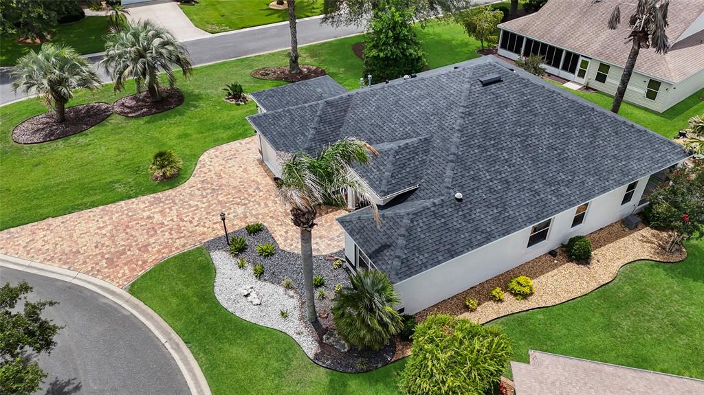 An aerial view shows a house with a dark shingled roof, paver driveway, and landscaping — 1718 MEANS LANE, THE VILLAGES, FL