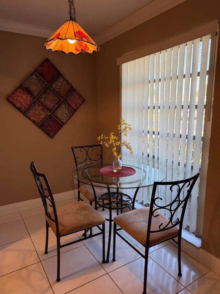 A dining nook features a glass table, three chairs, a stained-glass pendant light, and blinds — 8786 Belle Aire Drive, Boca Raton FL 33433, BOCA RATON, FL