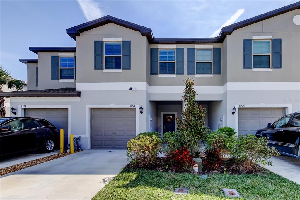 A multi-unit residential building features three garage doors, gray stucco walls, and blue shutters — 8294 CORNER PINE WAY, NEW PORT RICHEY, FL