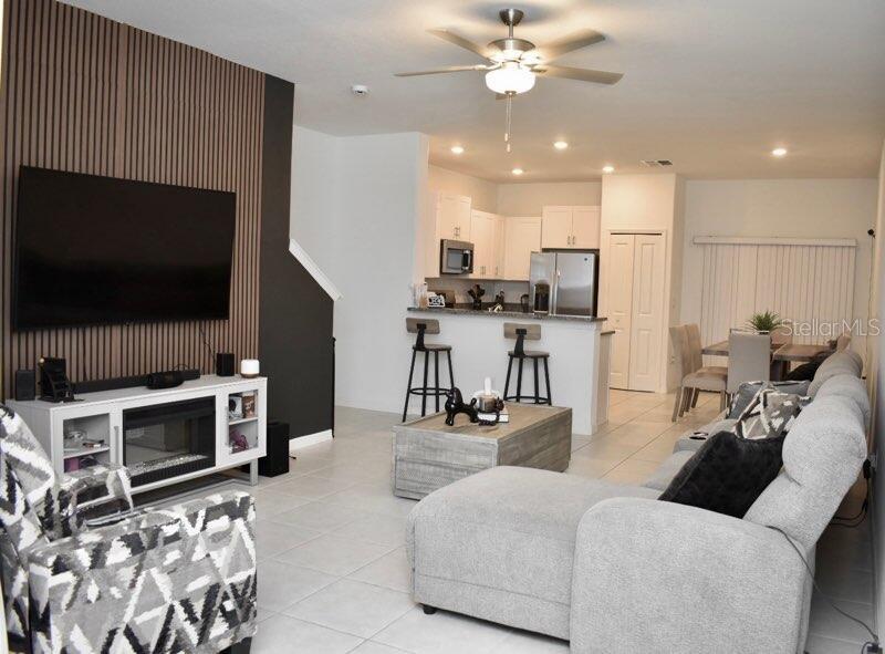 A living room with a fireplace and wood-slat wall opens to a kitchen with bar seating — 8294 CORNER PINE WAY, NEW PORT RICHEY, FL