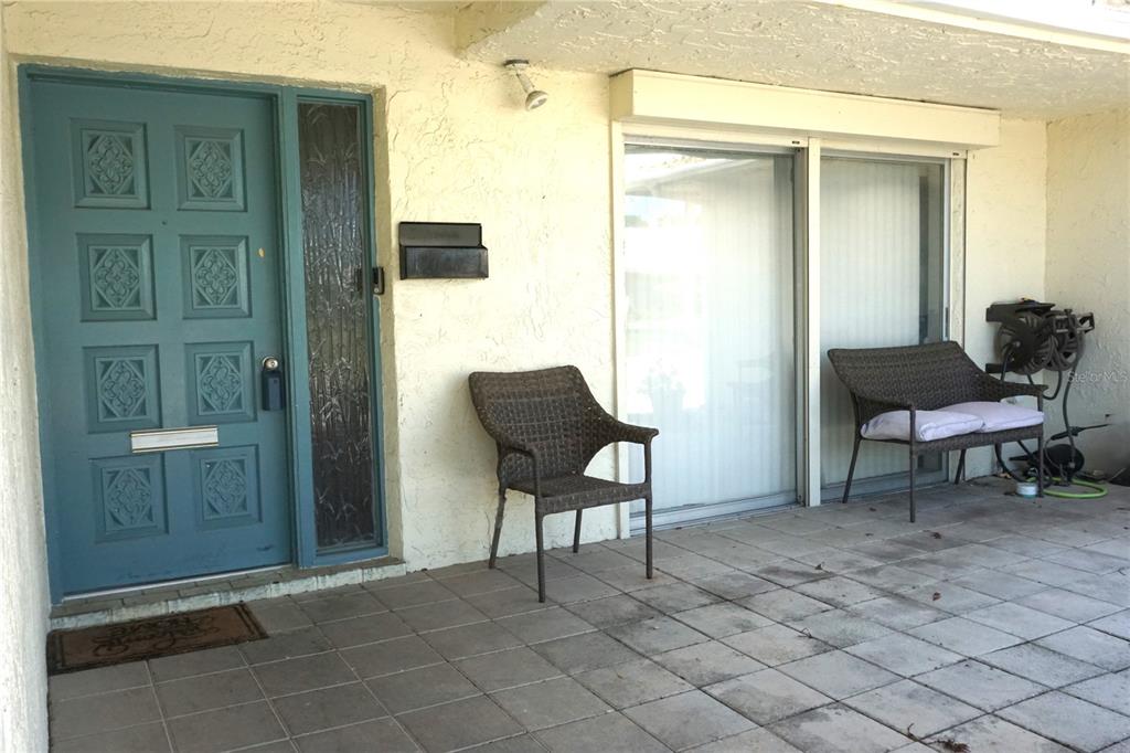 A patio area features a blue front door, sliding glass doors, and two wicker chairs — 10451 AZALEA PARK DRIVE N UNIT 2, PINELLAS PARK, FL