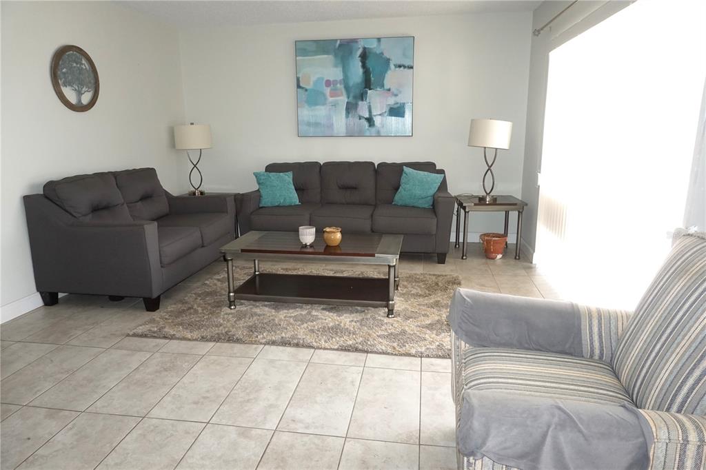 A living room features gray sofas, a coffee table, and a striped armchair on tile — 10451 AZALEA PARK DRIVE N UNIT 2, PINELLAS PARK, FL