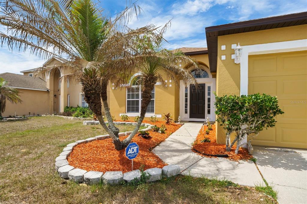 A yellow stucco house features a palm tree, orange mulch, and an ADT security sign — 140 MILESTONE DRIVE, HAINES CITY, FL