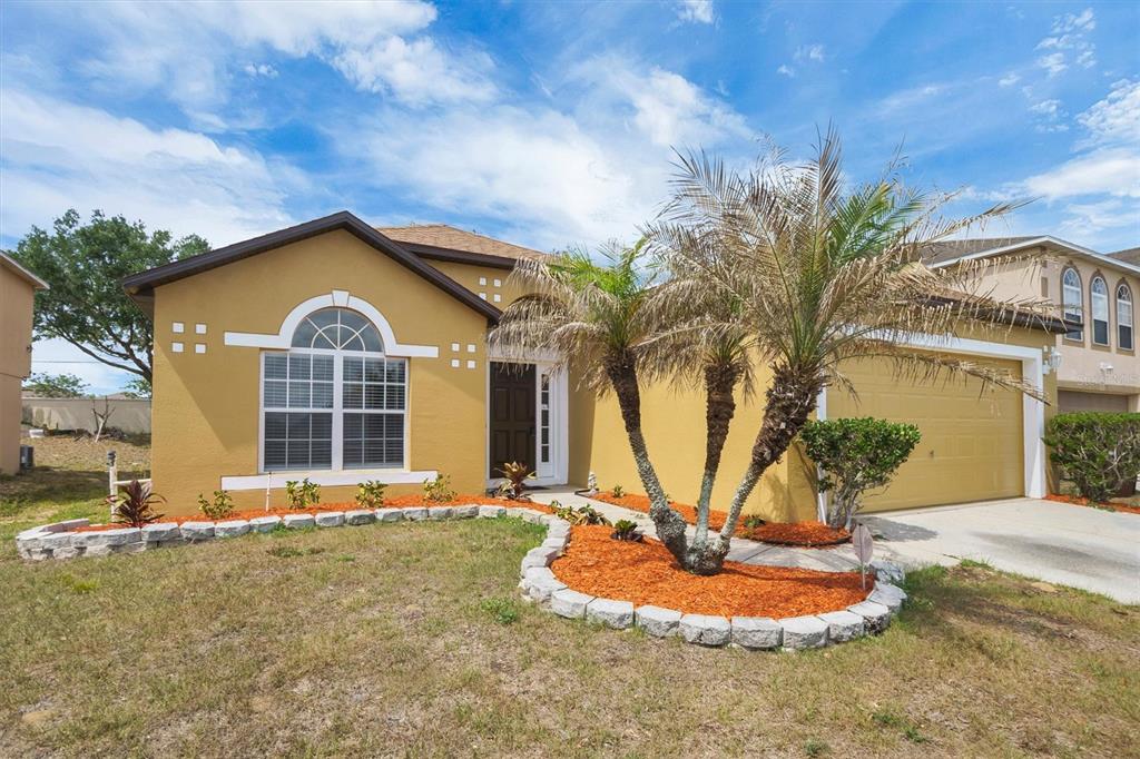 A single-story yellow house with a two-car garage and a landscaped front yard — 140 MILESTONE DRIVE, HAINES CITY, FL