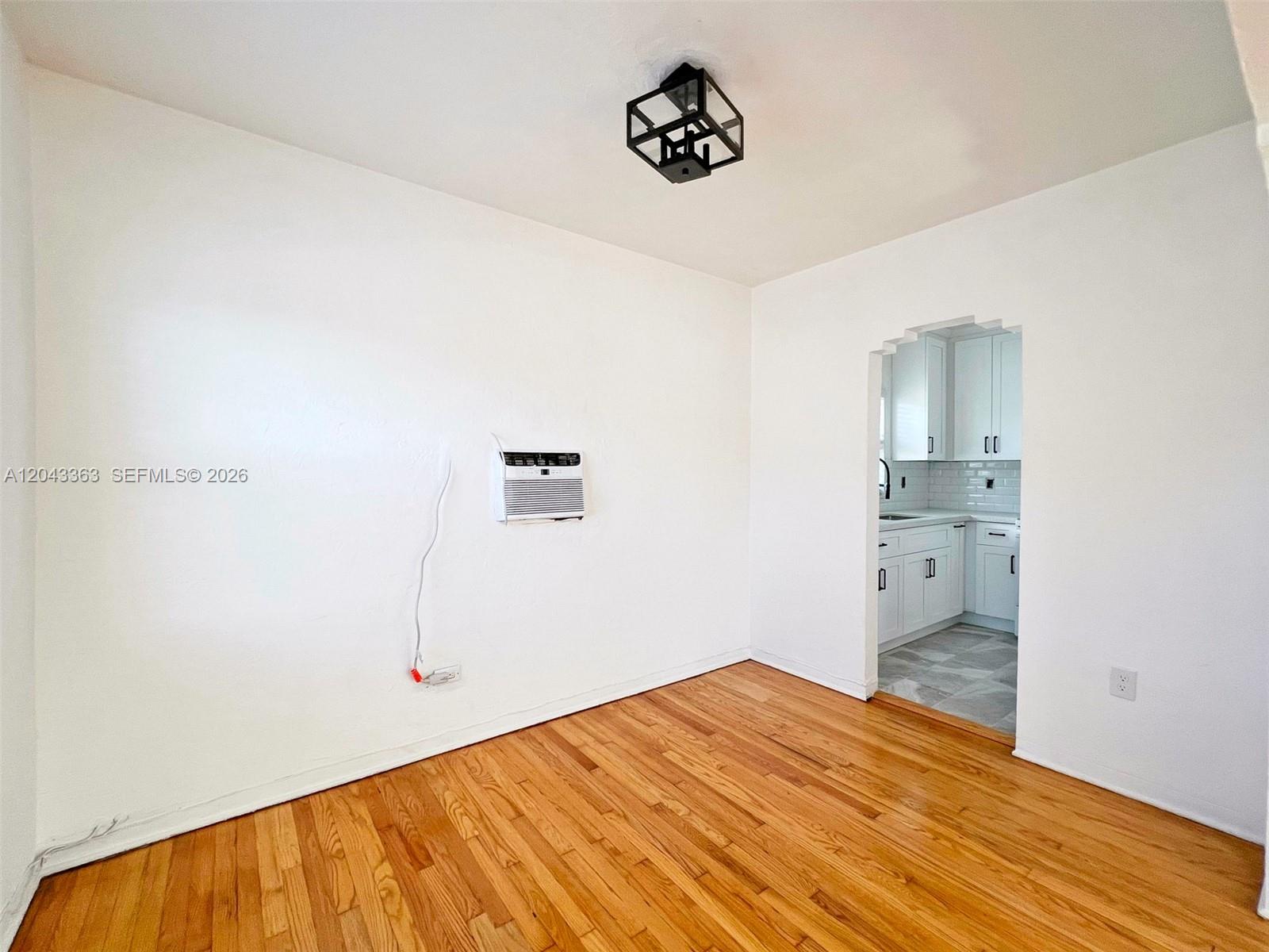 An empty room with hardwood floors, a wall-mounted air conditioner, and a doorway to a kitchen — 2102 SW 14 Ter # 1466, Miami FL 33145, MIAMI, FL