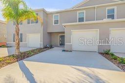 A two-story townhouse exterior with a concrete driveway, a palm tree, and two garage doors — 2723 SILVER CANOE DRIVE, EDGEWATER, FL