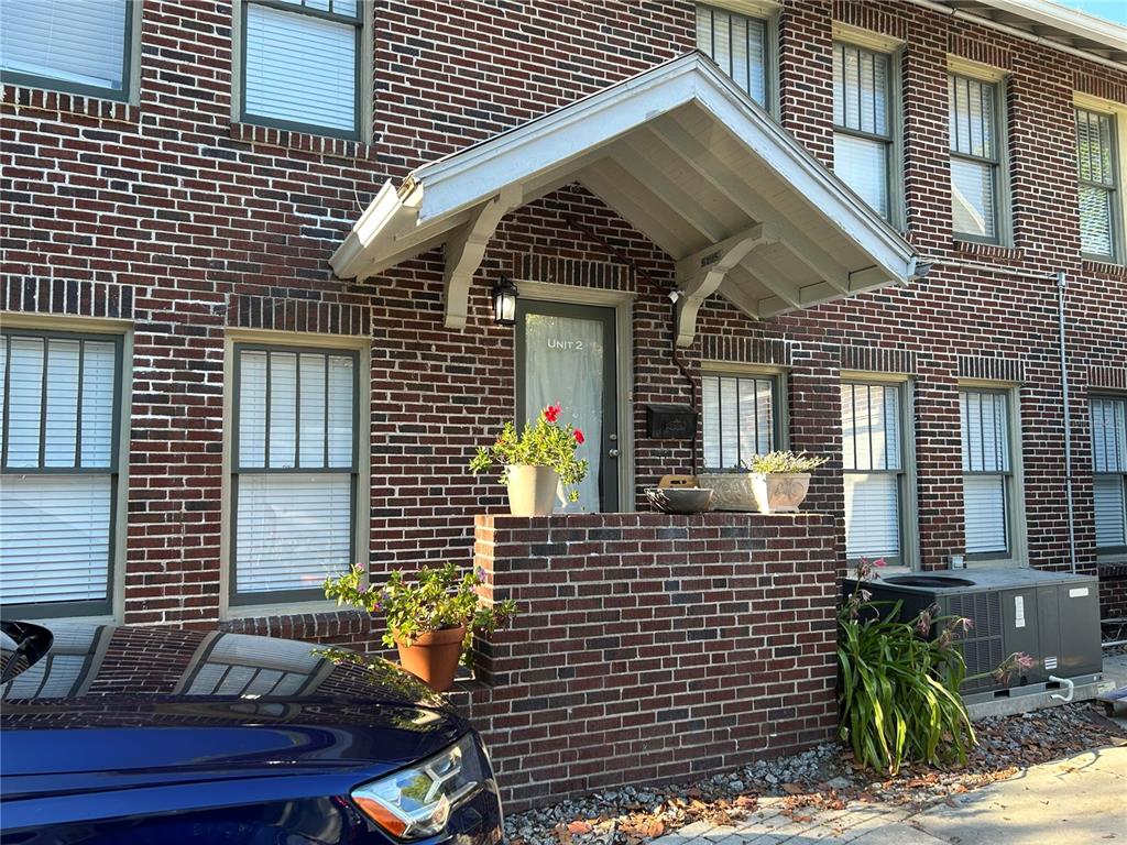 A brick building exterior features a covered entryway with a glass door labeled Unit 2 — 5205 N CENTRAL AVENUE, TAMPA, FL