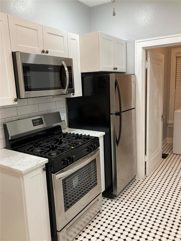 A kitchen features white cabinets, stainless steel appliances, and a black-and-white tiled floor — 5205 N CENTRAL AVENUE, TAMPA, FL