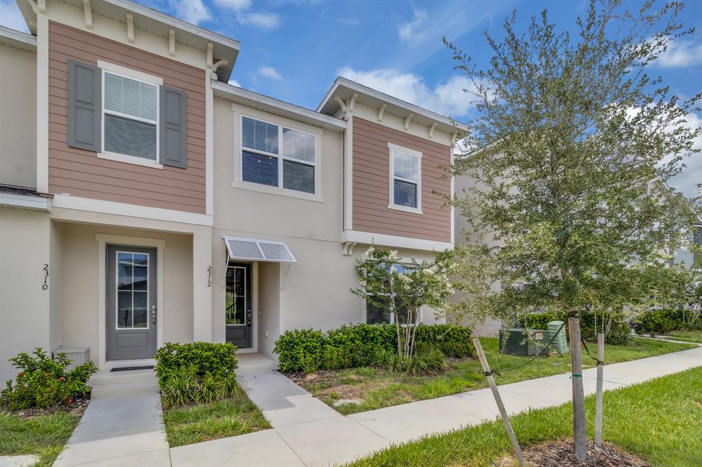 A two-story townhouse exterior features tan stucco, brown siding, and two front entry doors — 2312 ZABALLINA PLACE, KISSIMMEE, FL