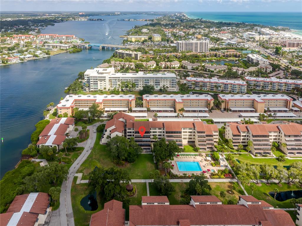 An aerial view shows a multi-story apartment complex with a pool near a waterway — 6267 MIDNIGHT PASS ROAD UNIT 306, SARASOTA, FL