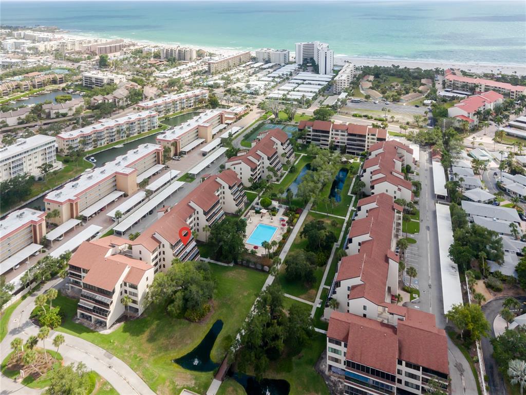 An aerial view of a multi-building apartment complex with a pool and nearby beach — 6267 MIDNIGHT PASS ROAD UNIT 306, SARASOTA, FL