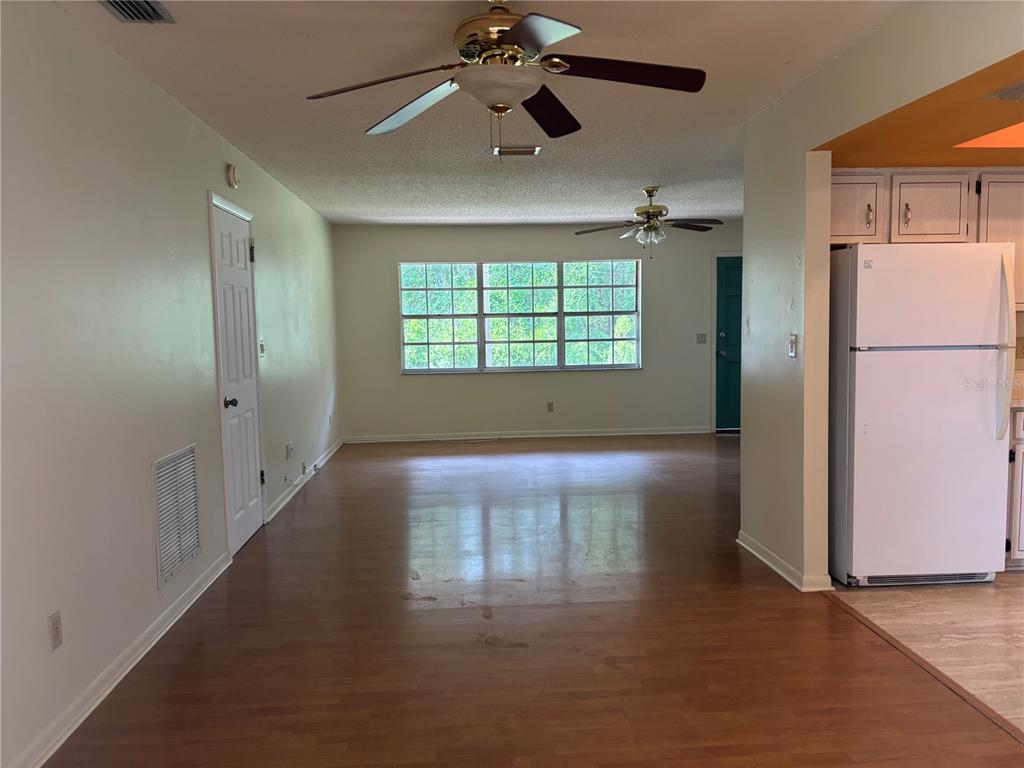 An open-concept living area features wood-look flooring, two ceiling fans, and a white refrigerator — 808 SPRUCE STREET, INVERNESS, FL