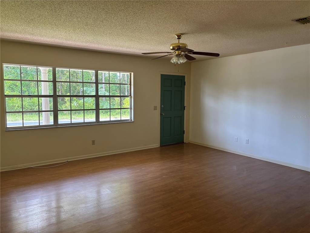 An empty room with wood-look flooring, a ceiling fan, a large window, and a door — 808 SPRUCE STREET, INVERNESS, FL