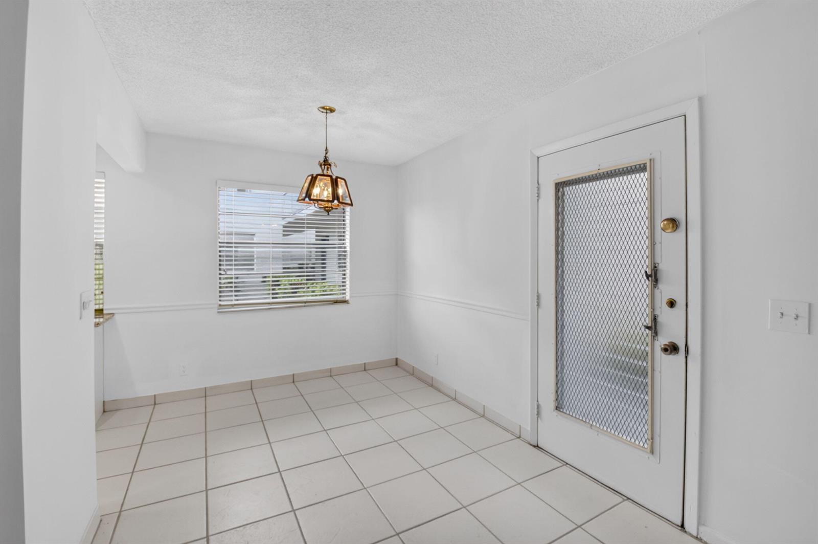 A dining area with white walls, tile flooring, a window with blinds, and a screen door — 200 Normandy E # 200, Delray Beach FL 33484, DELRAY BEACH, FL