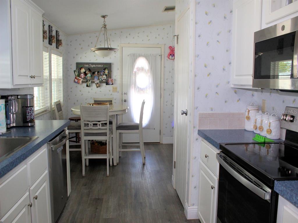 A kitchen with white cabinets, blue countertops, a dining area, and floral wallpaper — 64 THATCH PALM STREET W, LARGO, FL