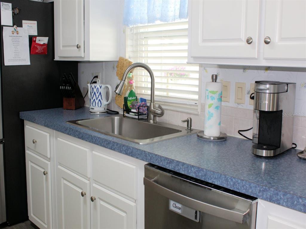 A kitchen features white cabinets, blue laminate countertops, a stainless steel sink, and a dishwasher — 64 THATCH PALM STREET W, LARGO, FL