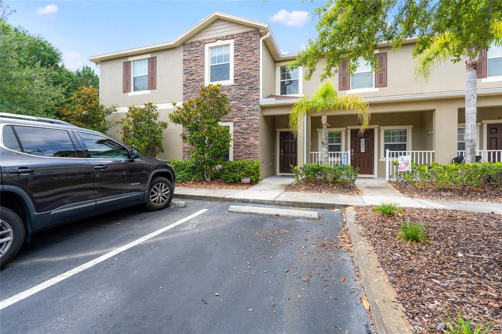 A two-story townhouse exterior features a stone facade, beige stucco, and a paved parking space — 31210 GOSSAMER WAY, WESLEY CHAPEL, FL