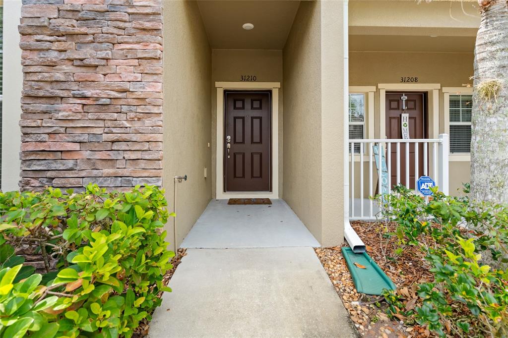 The exterior view shows two adjacent residential front doors with stone veneer and landscaping — 31210 GOSSAMER WAY, WESLEY CHAPEL, FL