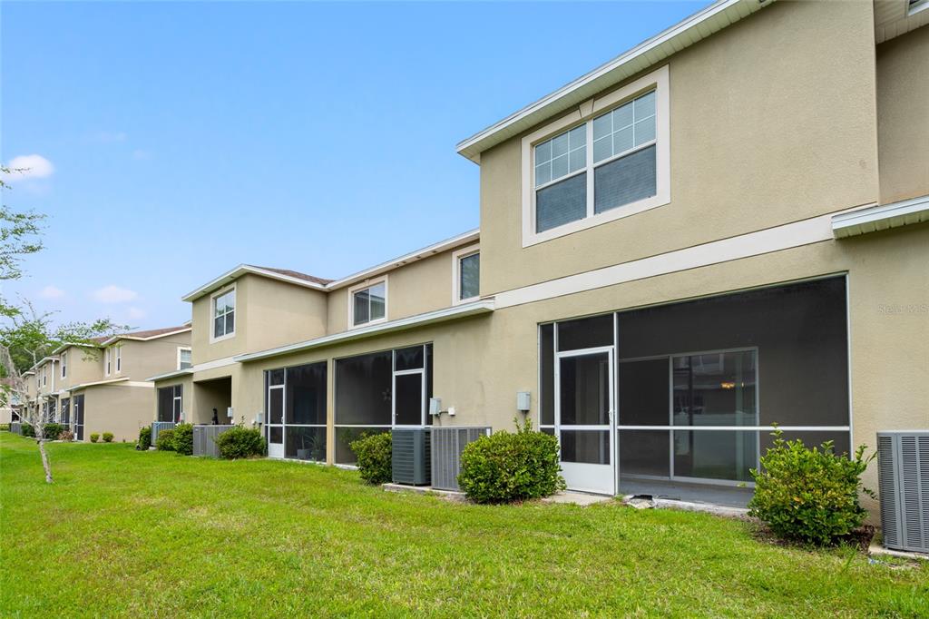 The exterior rear view of a multi-story townhouse complex features screened-in patios and green lawns — 31210 GOSSAMER WAY, WESLEY CHAPEL, FL