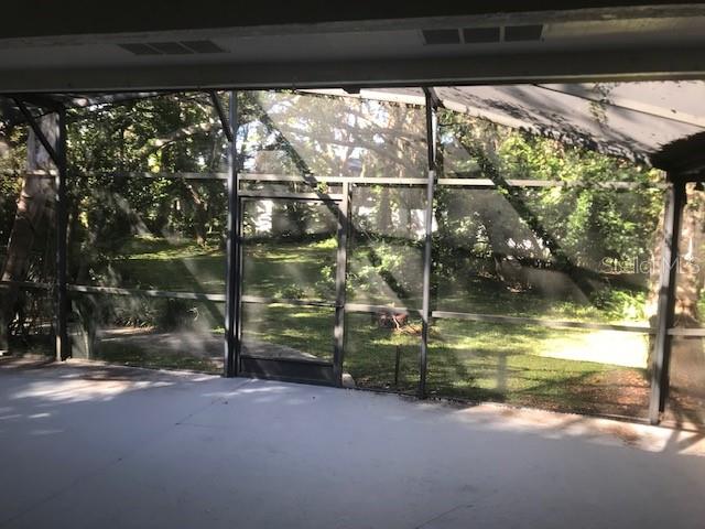 A view from a covered patio through a screened enclosure looking out toward a wooded yard — 300 SUN OAKS COURT, LAKE MARY, FL