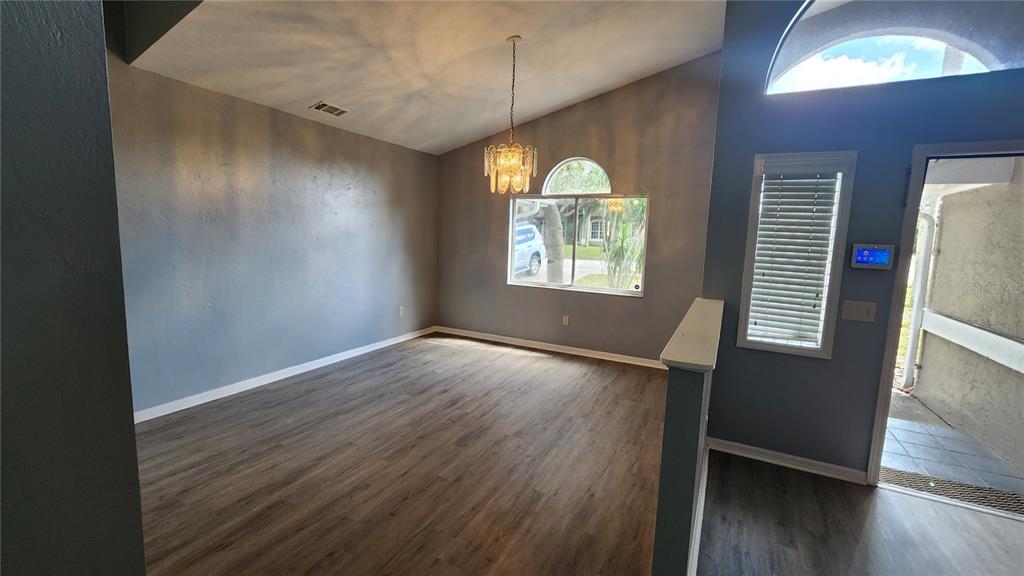 An empty room with wood-look flooring, a vaulted ceiling, a chandelier, and a large window — 300 SUN OAKS COURT, LAKE MARY, FL