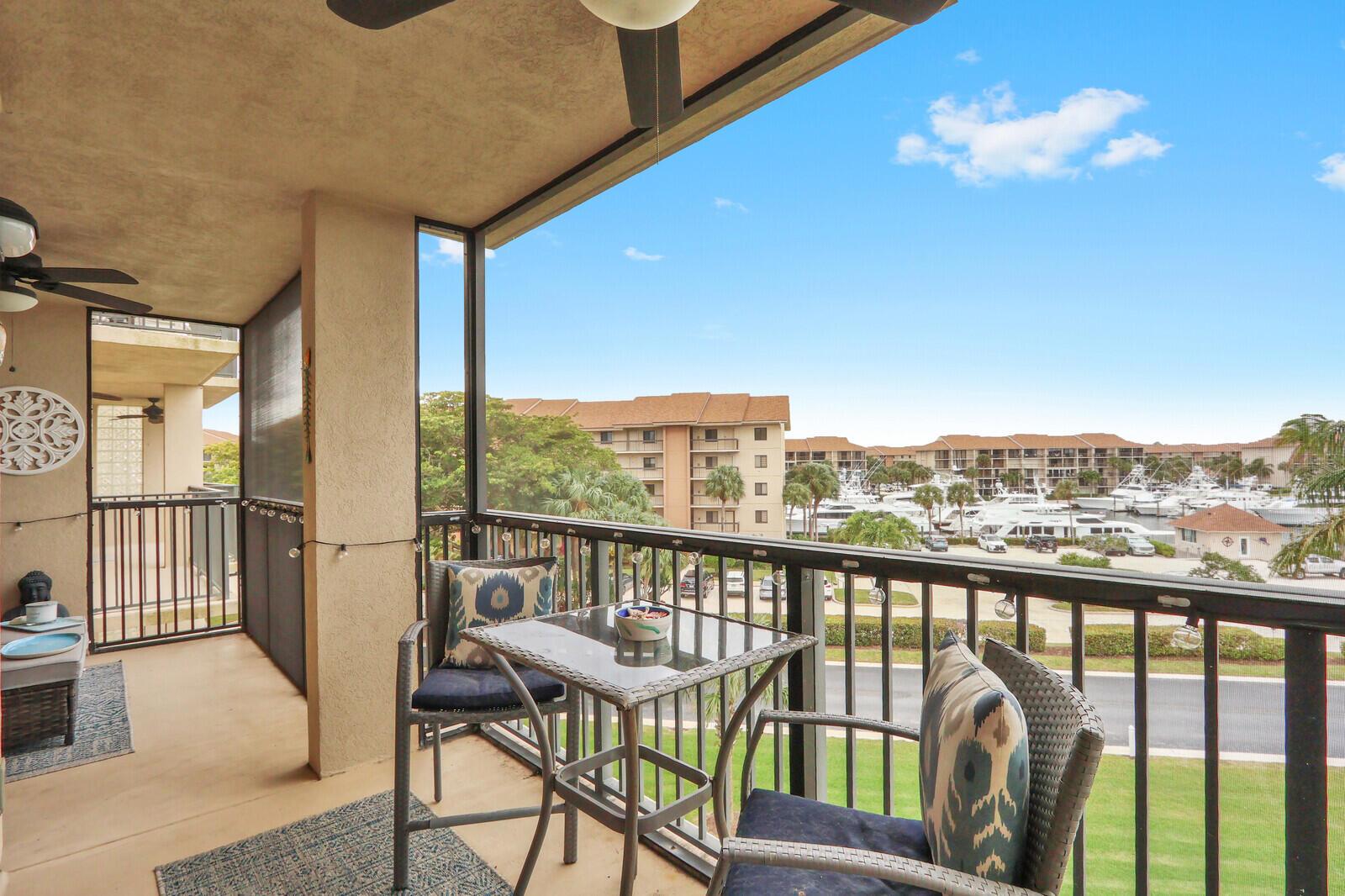 A screened balcony features a small glass table, two chairs, and a view of boats — 901 Seafarer Circle # 403, Jupiter FL 33477, JUPITER, FL