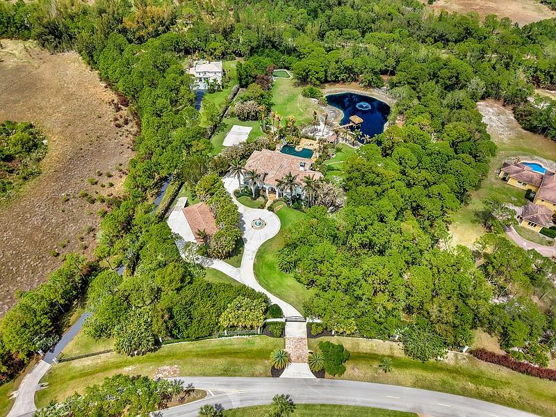 An aerial view shows a large house with a pool and pond surrounded by trees — 2584 SE RANCH ACRES CIRCLE, JUPITER, FL