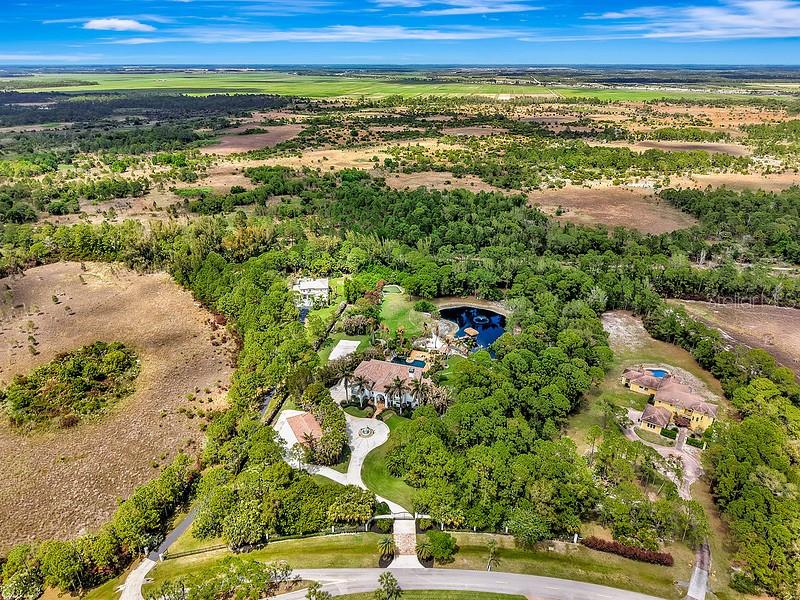 An aerial view shows a large estate with a pool and pond surrounded by trees — 2584 SE RANCH ACRES CIRCLE, JUPITER, FL