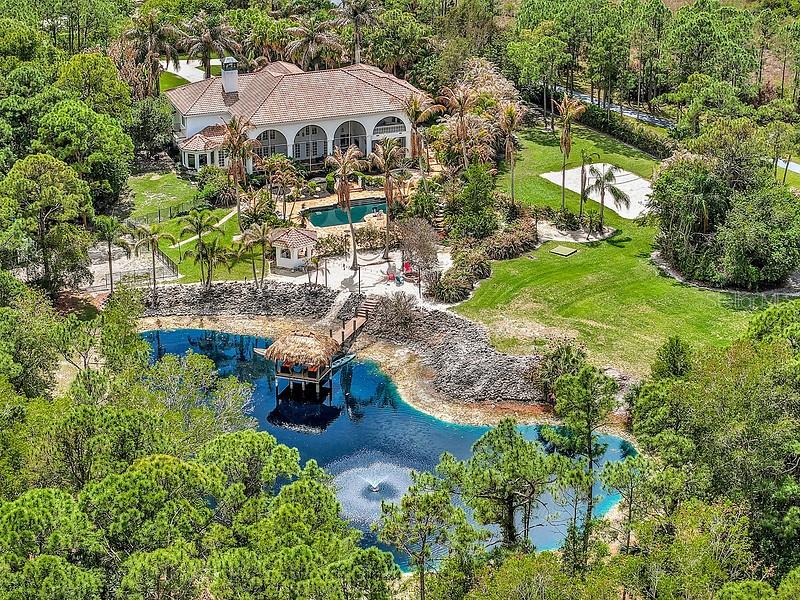 An aerial view shows a house with a pool, a pond, and a tiki hut — 2584 SE RANCH ACRES CIRCLE, JUPITER, FL