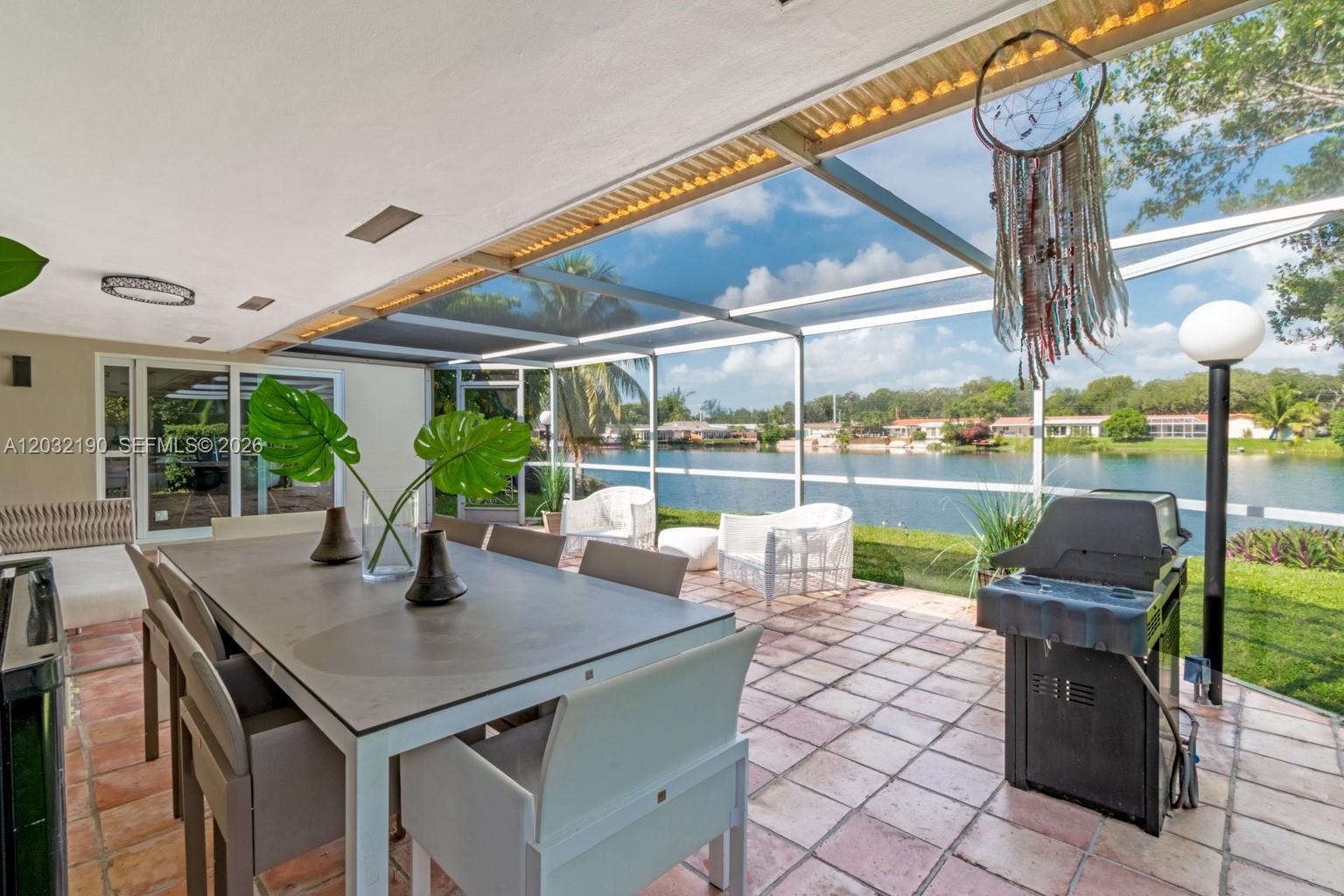 A covered patio with a dining set, grill, and screen enclosure overlooking a lake — 19950 NE 24th Ave # 1, Miami FL 33180, MIAMI, FL