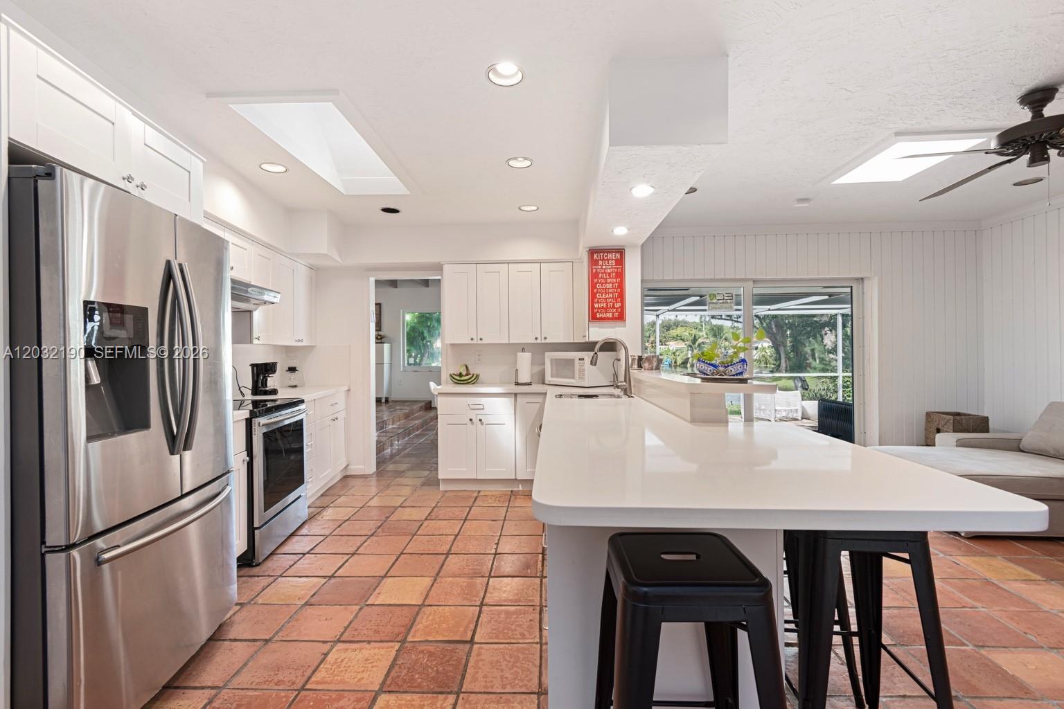 A kitchen features white cabinets, stainless steel appliances, a large island, and terracotta tile floors — 19950 NE 24th Ave # 1, Miami FL 33180, MIAMI, FL