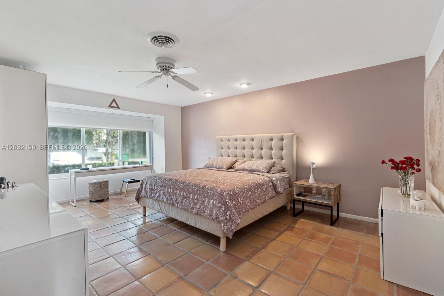 A bedroom features a tufted headboard, terracotta tile flooring, and a large window with desk — 19950 NE 24th Ave # 1, Miami FL 33180, MIAMI, FL