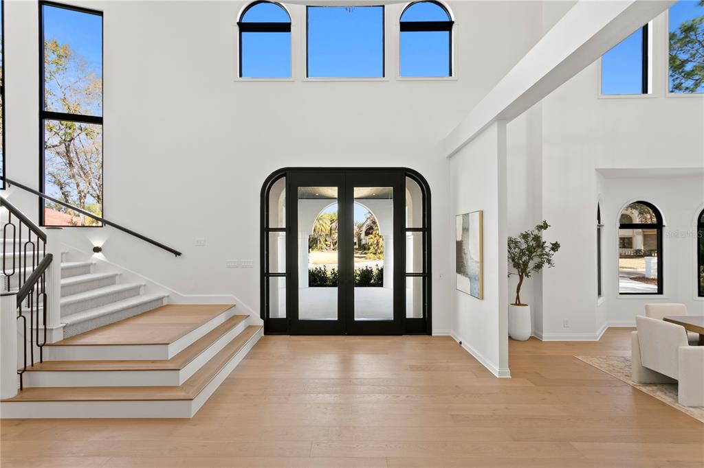 A bright, modern entryway features light wood floors, a grand staircase, and black-framed glass doors — 6324 W MACLAURIN DRIVE, TAMPA, FL